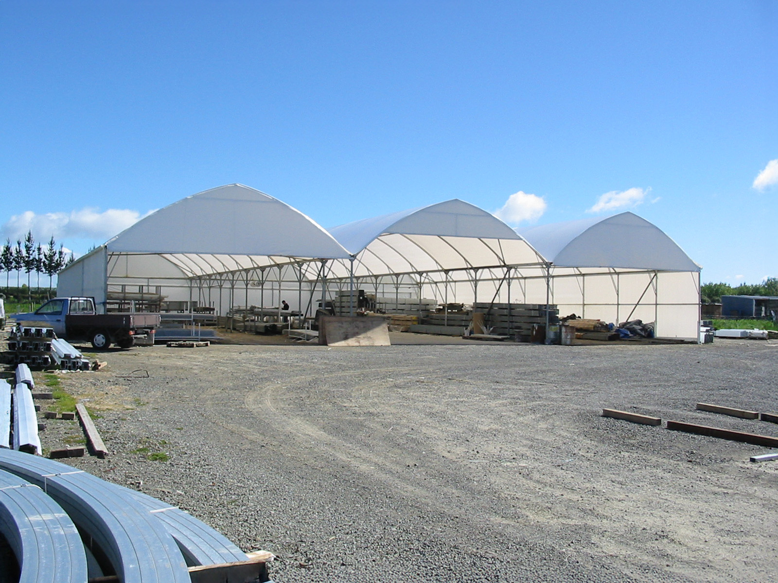 Three open industrial structures next to each other with blue sky and a large gravel path