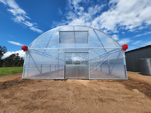 Front shot of greenhouse - blue sky with some clouds - on dirt ground